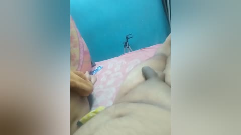 Video of a man's nude torso and erect penis on a pink and yellow bedspread, with a blue wall and a bicycle in the background.