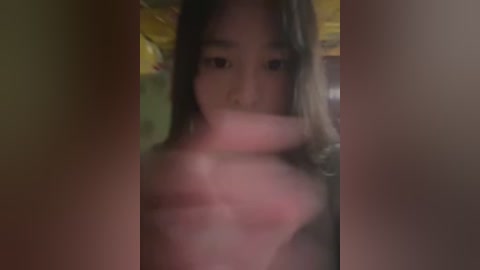 A blurry, dimly-lit video of an Asian woman with long black hair partially covering her face, holding a phone in front of her.