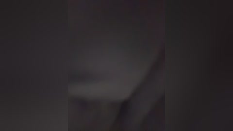 This image is a blurred video featuring a dimly lit, dark-haired individual with a partial facial view. The background is indistinct, and the lighting is low, making it difficult to discern specific details.