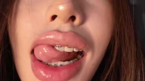 Close-up video of a young woman with fair skin, parted lips showing braces and a slightly open mouth. Her straight brown hair frames the top of the image.