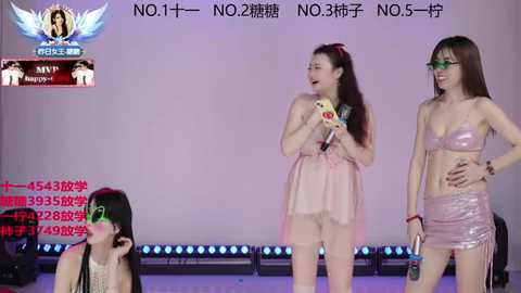 Video of three women singing on stage, wearing revealing outfits, with one in a pink dress and the others in skimpy pink and silver outfits. Background includes stage lights and Chinese text.
