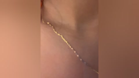 Close-up video of a delicate, thin gold chain necklace draped across a person's bare, light-skinned neck, with the background blurred and warm-toned.