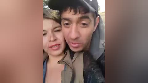 Video of a man and woman with dark hair, wearing casual clothing, embracing outdoors, with blurred background.