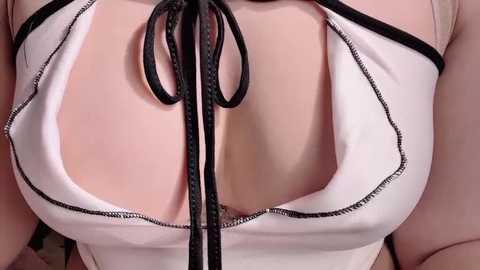 Video of a close-up of a woman's cleavage in a low-cut, white blouse with black lace trim and a black ribbon bow, highlighting her ample breasts and fair skin.