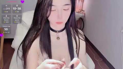 Video of an East Asian woman with long black hair, wearing a black choker and a white top, sitting in a chair, applying makeup, with a digital overlay showing streaming stats.