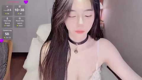 Video of an Asian woman with long black hair, wearing a black choker and a white lace bra, seated indoors, with virtual social media stats overlaid.