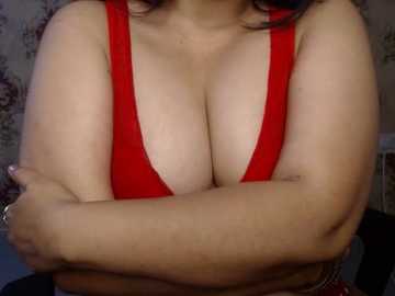 Video of a light-skinned woman with large breasts, wearing a red bra, arms crossed, and a floral-patterned background.