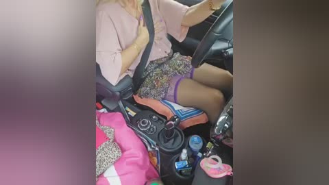 Media: Video of a woman in a car, wearing a pink blouse and leopard-print skirt, driving with a pink handbag on her lap.