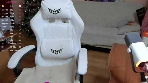 A video of a white gaming chair with a \"G\" logo, positioned in a living room with a couch, Christmas tree, and a white gaming headset in the foreground.