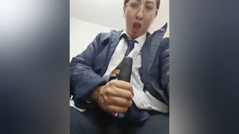 Video of a shocked Asian man in a dark blue suit, white shirt, and tie, holding a gun, with blurred background.