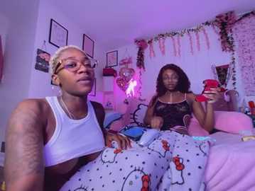 Video of two Black women, one with short blonde hair, the other with long black hair, lounging on a bed in a pink room with fairy lights and cartoon sheets.
