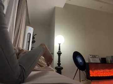 Media: Video of a person in a hospital bed, wearing a light-colored shirt, holding a remote control, with a white lamp and a TV with a red screen in the background.