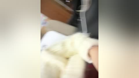 Blurry video of a person wearing a white shirt and light-colored pants, sitting in a dark car with a blurry background, possibly a driver's seat.