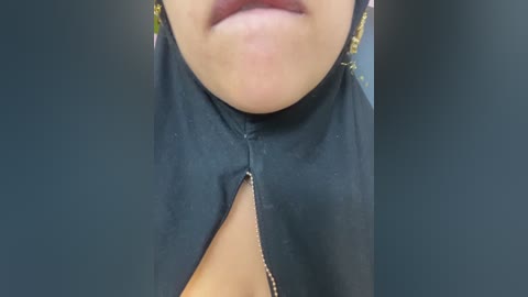 Video of a close-up of a person's lower face, showing a dark green surgical gown with a slit neckline, revealing a hint of cleavage, and a pair of lips slightly parted.