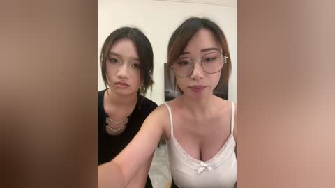 Video of two East Asian women with short hair, one wearing a black top and necklace, the other in a white tank top with glasses.