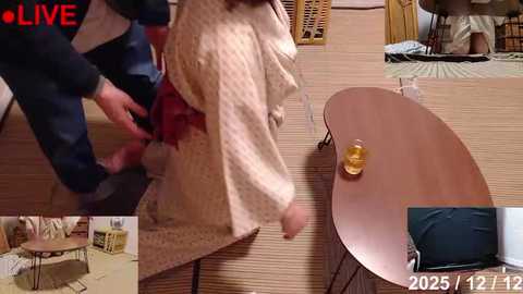 Video of a man in a striped robe kneeling to tie a black woman's shoe, taken in a Japanese-style room with a wooden floor, round table, and traditional decor.