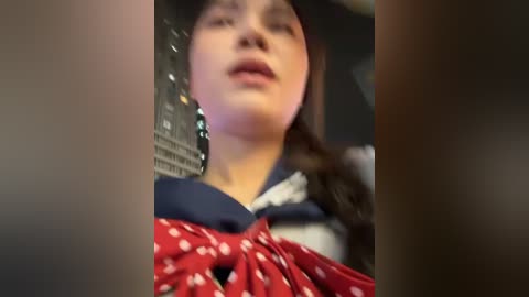 A blurred video of a young woman in a dark blue sailor dress with a red polka-dot scarf, wearing a black hat, with a dimly lit background.