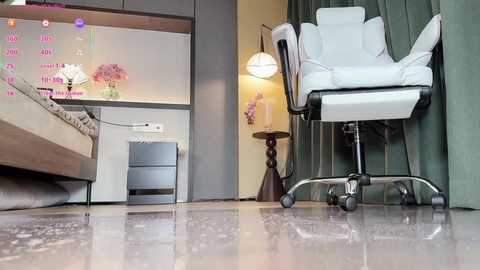 Video of a modern, minimalist bedroom with a white recliner chair, a small wooden side table, and a beige bed against a light green wall.