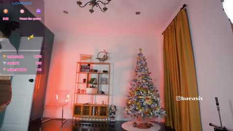 Video of a cozy, dimly lit living room with a Christmas tree adorned with colorful ornaments, a beige chair, and mustard-yellow curtains.