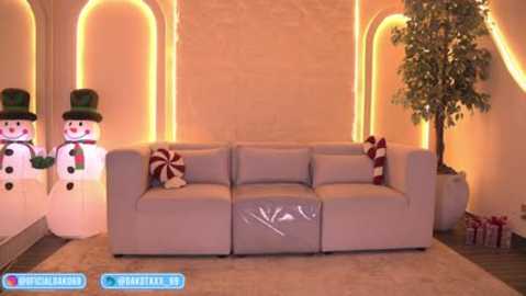 Video of a festive living room with a beige sectional sofa, adorned with red and white striped pillows. Snowmen and a Christmas tree decorate the walls, creating a cozy, holiday atmosphere.