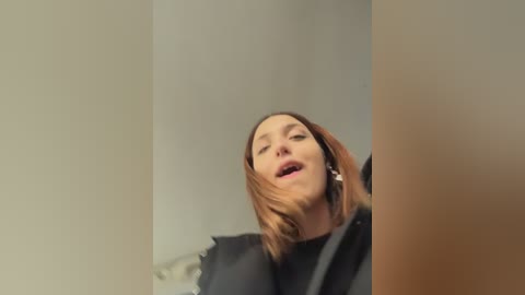 Video of a young Caucasian woman with straight, shoulder-length brown hair, wearing a black top, slightly tilted head back in apparent pleasure, blurred background.