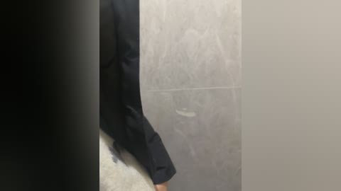 A video of a person in a black suit standing next to a concrete wall, with a blurred black object on the left side of the image.