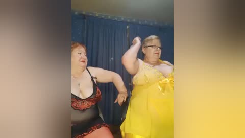 Video of two plus-sized women in lingerie, one in a red lace bra and the other in a yellow nightgown, dancing energetically in a dimly lit room with blue curtains.