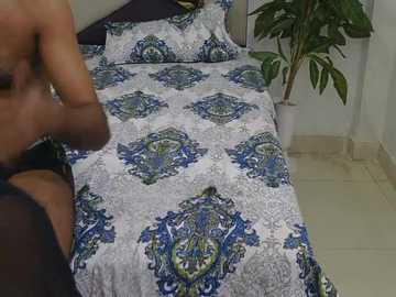 Video of a woman in a dark blue bra, standing near a bed with a white and blue paisley-patterned duvet cover.