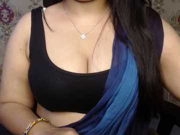 Video of a South Asian woman with medium brown skin, wearing a black sports bra and a blue sari, adorned with a gold bracelet and a silver necklace.