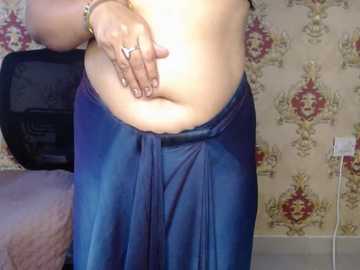 Video of a person with light skin, wearing a blue satin skirt, touching their stomach with both hands, in a room with floral wallpaper and a black TV.