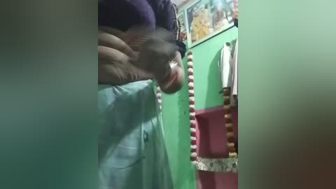 A video of a person in a small, colorful bathroom with green walls, wearing a dark shirt and holding a large, red, textured object, possibly a hair dryer.