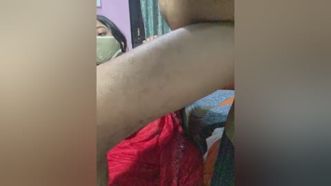 Video of a woman in a red saree, partially obscured by a beige curtain, with a visible arm, green mask, and partially visible face.