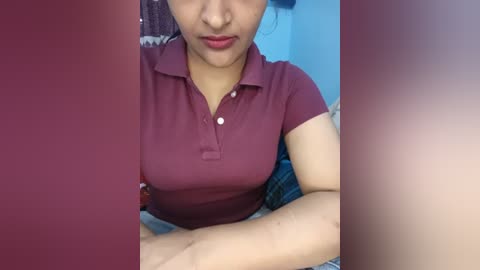 Video of a woman in a maroon polo shirt, arms crossed, leaning forward, slightly blurred, with a red and blue background.