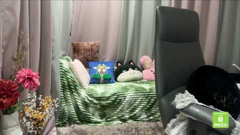 A video depicts a cozy room with a green-striped couch, pillows, and a fluffy cat. A tall black cat sits on a gray chair, while pink flowers and a vase add a touch of color.