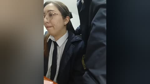 Video of a young Asian woman in a dark navy school uniform with a white shirt and black tie, standing next to a uniformed officer.