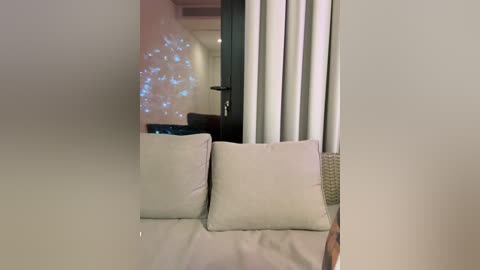 A video captures a modern, minimalist room with beige furniture and curtains. A wicker basket sits on a table, and a blue string of fairy lights adorns the wall.