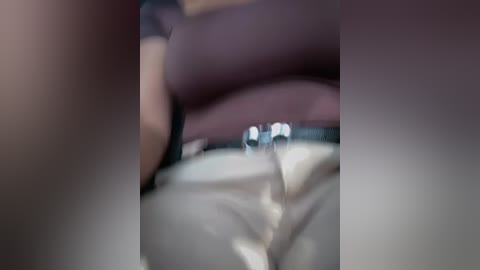 Video of a close-up view of a person's lower abdomen, with a clear fluid (possibly urine) trickling down. The skin tone is light, and the background is out of focus, featuring a blurred pink and brown fabric.