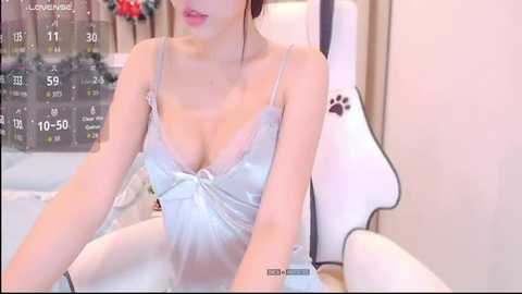 Video of an Asian woman in light blue lingerie, sitting on a white chair, with a guitar and a cat poster in the background.