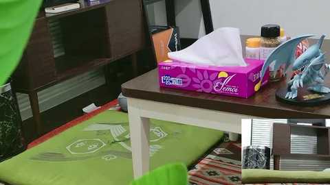 Video of a cluttered office desk with a box of Kleenex, a water bottle, and a colorful folder. Background includes a green mat and a partially visible person.