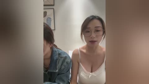 Media: Video of two Asian women in a hallway, one in glasses, denim jacket, the other in a white lace camisole, framed by blurred, masculine figures.