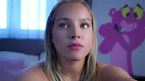 Media: Video of a young, light-skinned blonde woman with straight hair, wearing a pink top, looking thoughtful, in a bedroom with a pink cartoon character on the wall.