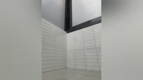 Media: Video of a corner room with white textured tile walls, a black ceiling beam, and light-colored marble flooring. The space has a modern, minimalist aesthetic with clean lines and neutral tones.