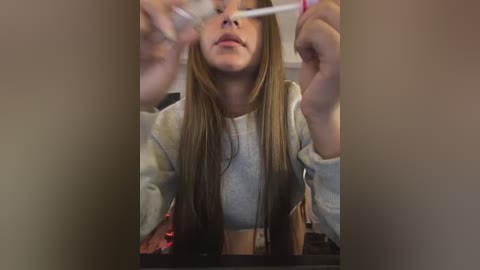 Media: A video of a young woman with straight, light brown hair, wearing a gray sweater, brushing her teeth in a bathroom. The image is blurry and out of focus.
