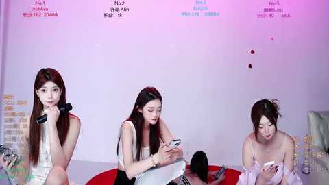 Video of three East Asian women with long, straight black hair, wearing sleeveless tops, seated on a red circular cushion, focused on smartphones, in a minimalist, white room with Chinese text.