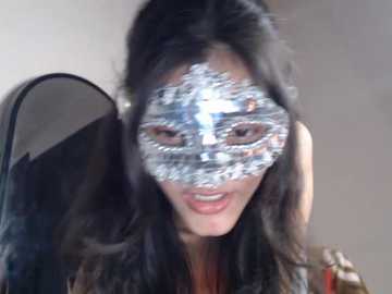 Video of an Asian woman with long black hair, wearing a silver Venetian mask, smiling. She has fair skin and is indoors.