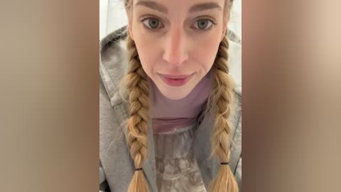 Video of a blonde woman with fair skin, blue eyes, and braided hair, wearing a gray sweater, taken from a close-up angle.