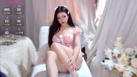 Video of an East Asian woman with long black hair, fair skin, and red lipstick, wearing a pink floral dress, sitting on a white chair in a softly lit, elegant room.
