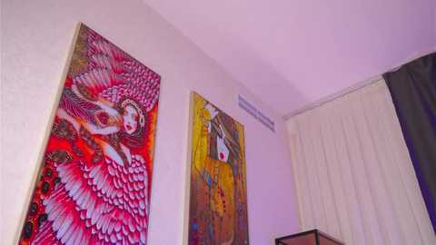 Video of a modern, minimalist room with a large, vibrant, abstract painting of a woman with red hair and wings on a white wall. A beige curtain covers a window on the right.