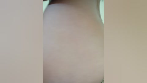 A close-up video of a nude female torso with a small, light-brown mole on the right side. The skin tone is pale, and the background is a soft, neutral beige, providing a subtle, unobtrusive setting.