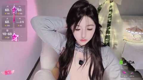 Media: Video of a young East Asian woman with long black hair, wearing a grey top, lying on a white couch, in a cozy, softly lit room.